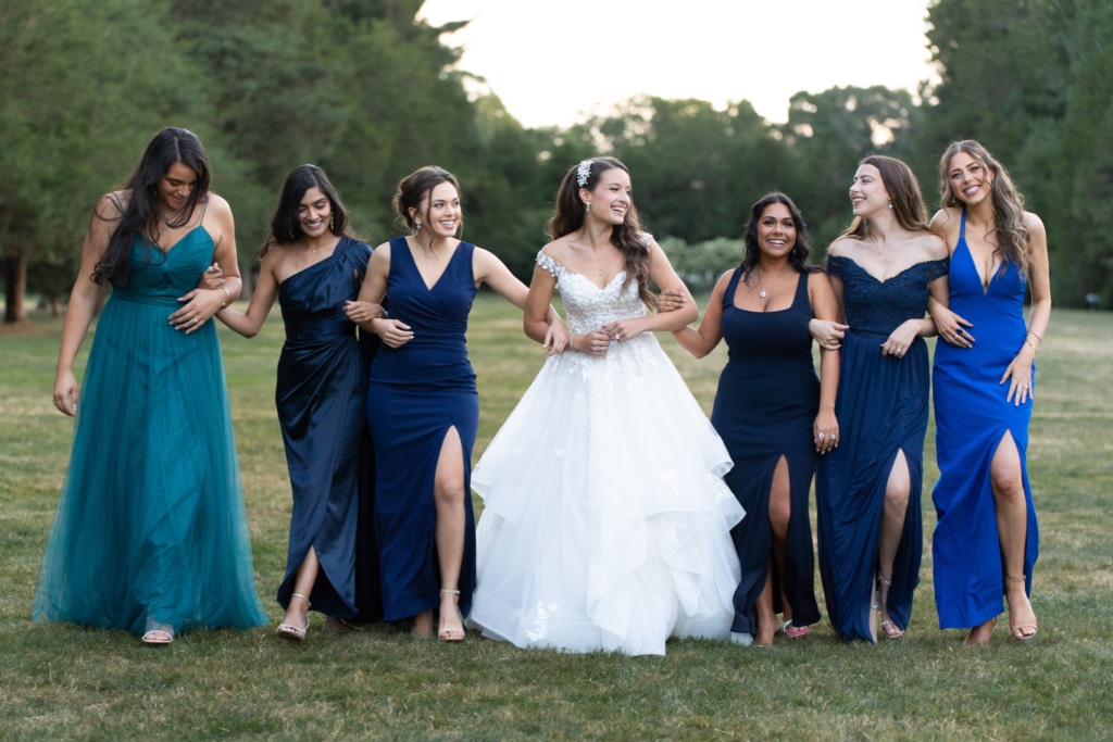 a bride walks with linked arms with her bridesmaids