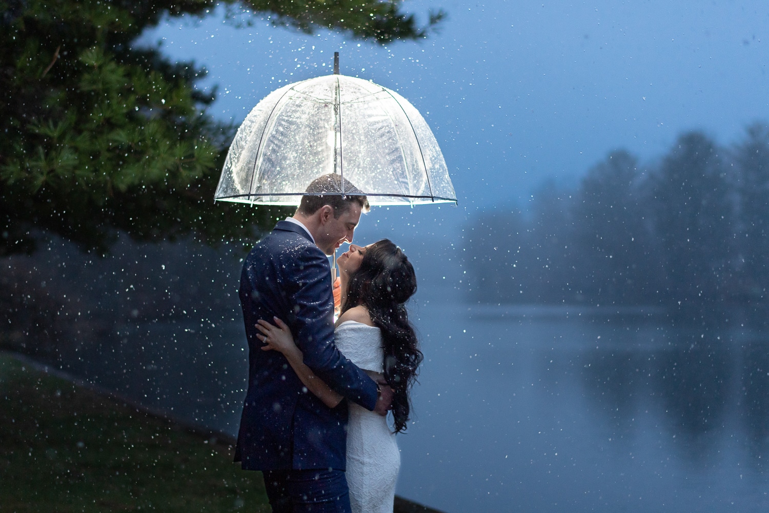 a bride and groom in the snow under an umbrella by a lake