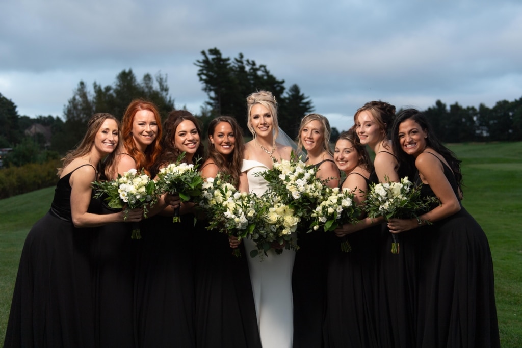Bridesmaids in black dresses and a bride in a white dress pose with their bouquets.
