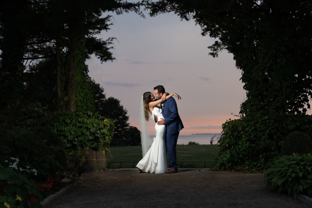 a bride and groom kiss while the sun sets behind them