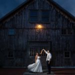 a groom twirls a bride in her wedding dress outside the barn