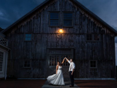 a groom twirls a bride in her wedding dress outside the barn