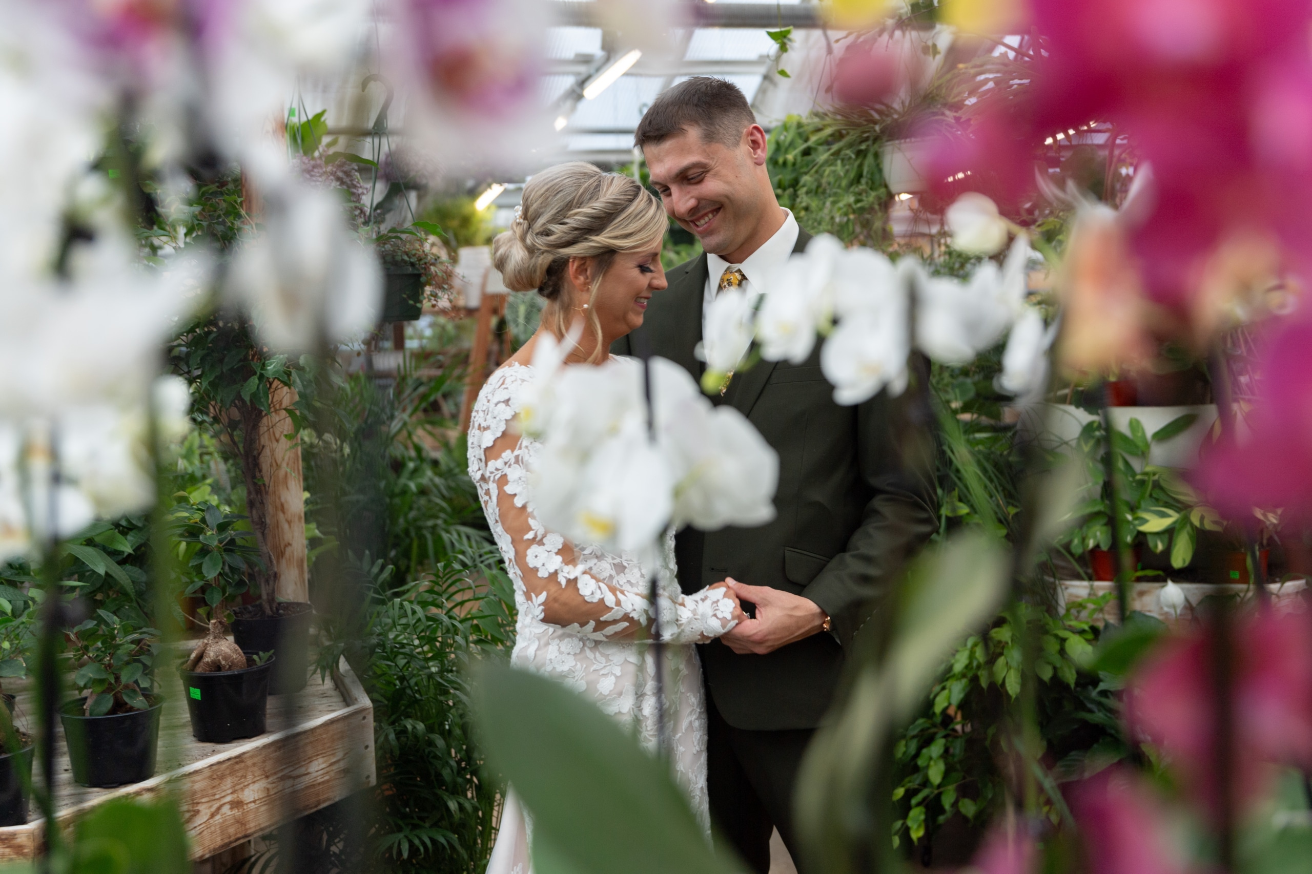 bride and groom hold hands in a greenhouse surrounded by flowers